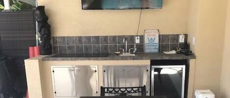 Un comedor con una mesa y sillas negras, un televisor montado en la pared y un salpicadero de azulejos.