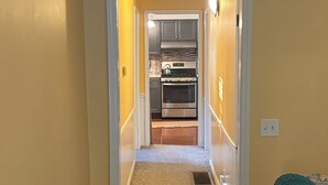 A hallway leading to a kitchen with a stove, oven, and cabinets.
