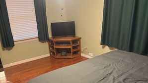 A bedroom with a bed, wooden flooring, a TV stand, and a window with curtains.