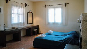 Ein Zimmer mit zwei Betten, einem Holztisch, einem Spiegel und einem Fenster mit Vorhängen.