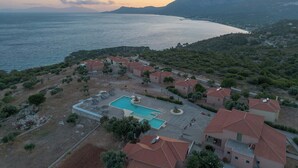 Eine Luftaufnahme eines Küstenresorts mit Villen, einem Schwimmbad und Blick auf Meer und Berge.