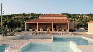 A pool area with a building in the background, surrounded by plants and a hilly landscape. - Intimate Studio w Garden and Inviting Shared Pool (Samos)