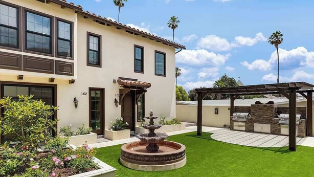 Un bâtiment à deux étages doté d’un patio comprenant une fontaine, une pergola et un espace barbecue extérieur.