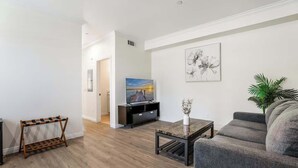 Un salon avec un canapé gris, une table basse, un téléviseur posé sur un meuble noir et un tableau accroché au mur.
