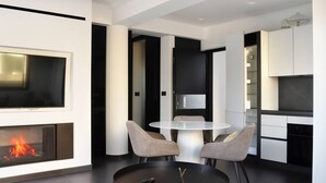 Un salon moderne avec une cheminée, une table ronde entourée de chaises, un téléviseur fixé au mur et un coin cuisine.