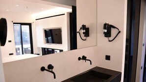 Une salle de bain moderne avec un grand miroir, un téléviseur encastré et un lavabo noir.