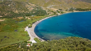 Luchtbeeld van een kustgebied met een strand, helderblauw water en omliggende begroeiing.