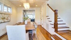 A dining area with a wooden table and chairs, a chandelier, and a staircase with wooden steps. - Walk to 12 South: Getaway w/ Outdoor Dining! (Nashville)