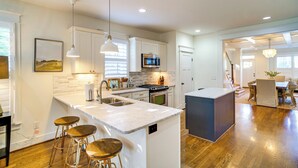 A modern kitchen with white cabinetry, a central island with stools, stainless steel appliances, and pendant lighting. - Walk to 12 South: Getaway w/ Outdoor Dining! (Nashville)