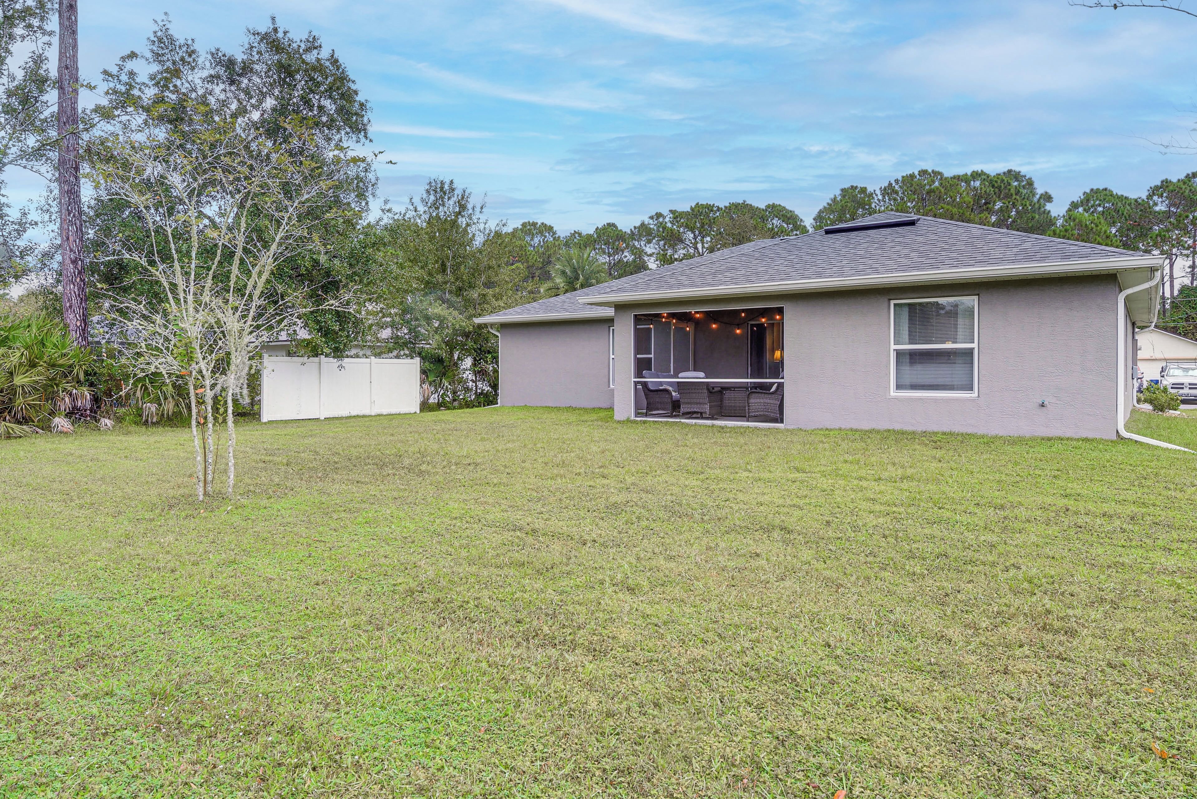 A single-story house with a covered patio area, a fenced yard, and a tree.