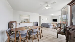 A modern living space with a dining area, a sofa, a television, and a ceiling fan.