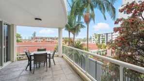 Een balkon met een tafel en stoelen, met uitzicht op een woonwijk met rode pannendaken en palmbomen.
