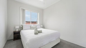 A hotel room with a large bed, a nightstand, a window, and a view of buildings outside.