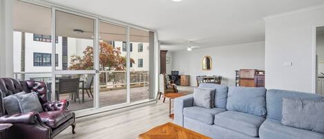 Een ruime woonkamer met een grote schuifpui naar een balkon, een leren fauteuil, een blauwe bank en een houten salontafel.