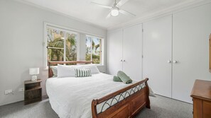 Een slaapkamer met een bed, nachtkastje, raam, plafondventilator en een kledingkast.