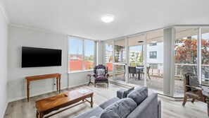 A spacious living room with a flat-screen TV, a wooden bench, a grey sofa, and a leather armchair.