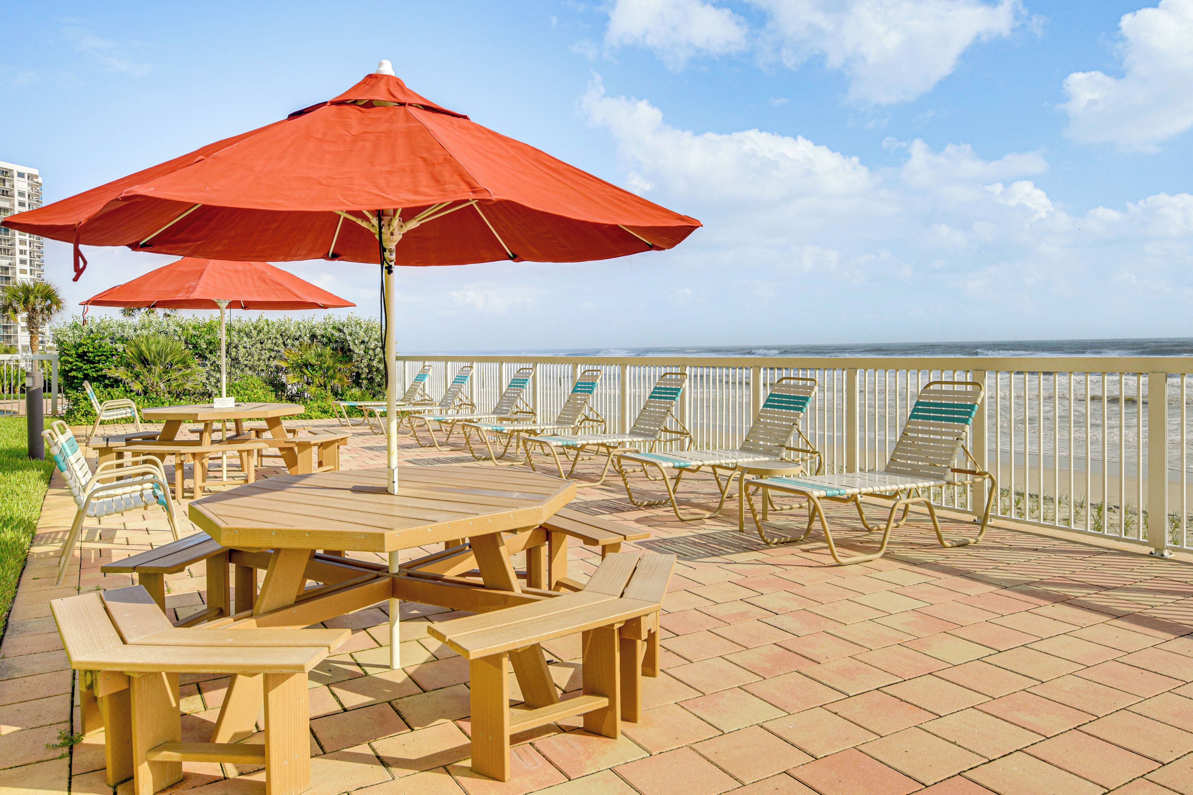 Une terrasse extérieure avec des tables de pique-nique et des chaises longues, donnant sur une étendue d’eau.