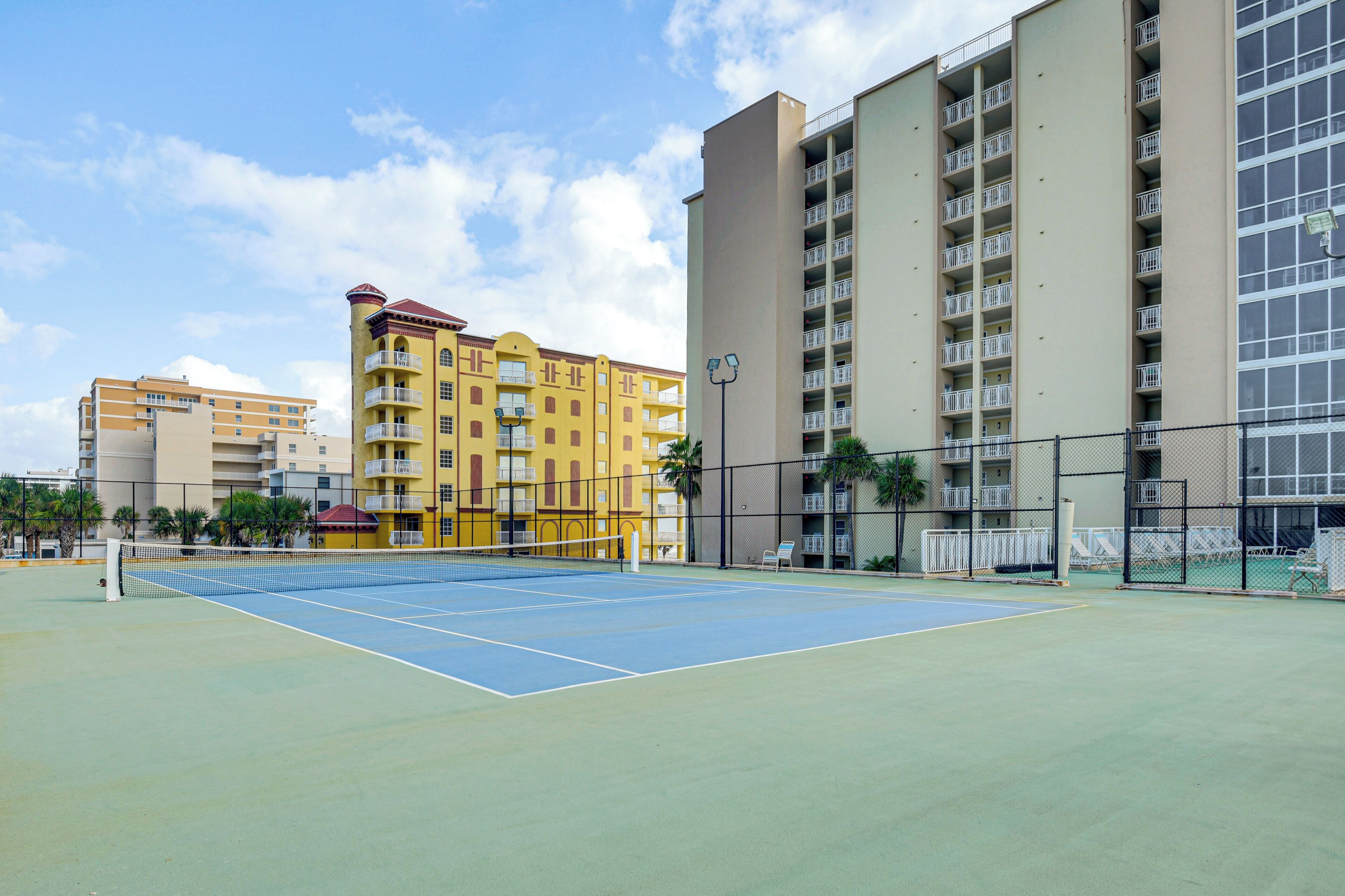 Cancha de tenis exterior con red, rodeada por edificios de varios pisos con balcones.