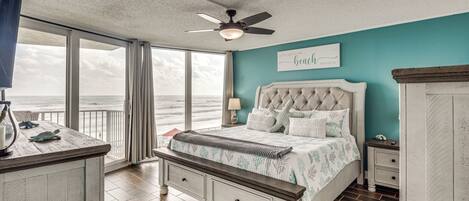 A bedroom with a view of the ocean, a ceiling fan, a bed with a headboard, and a nightstand with a lamp.