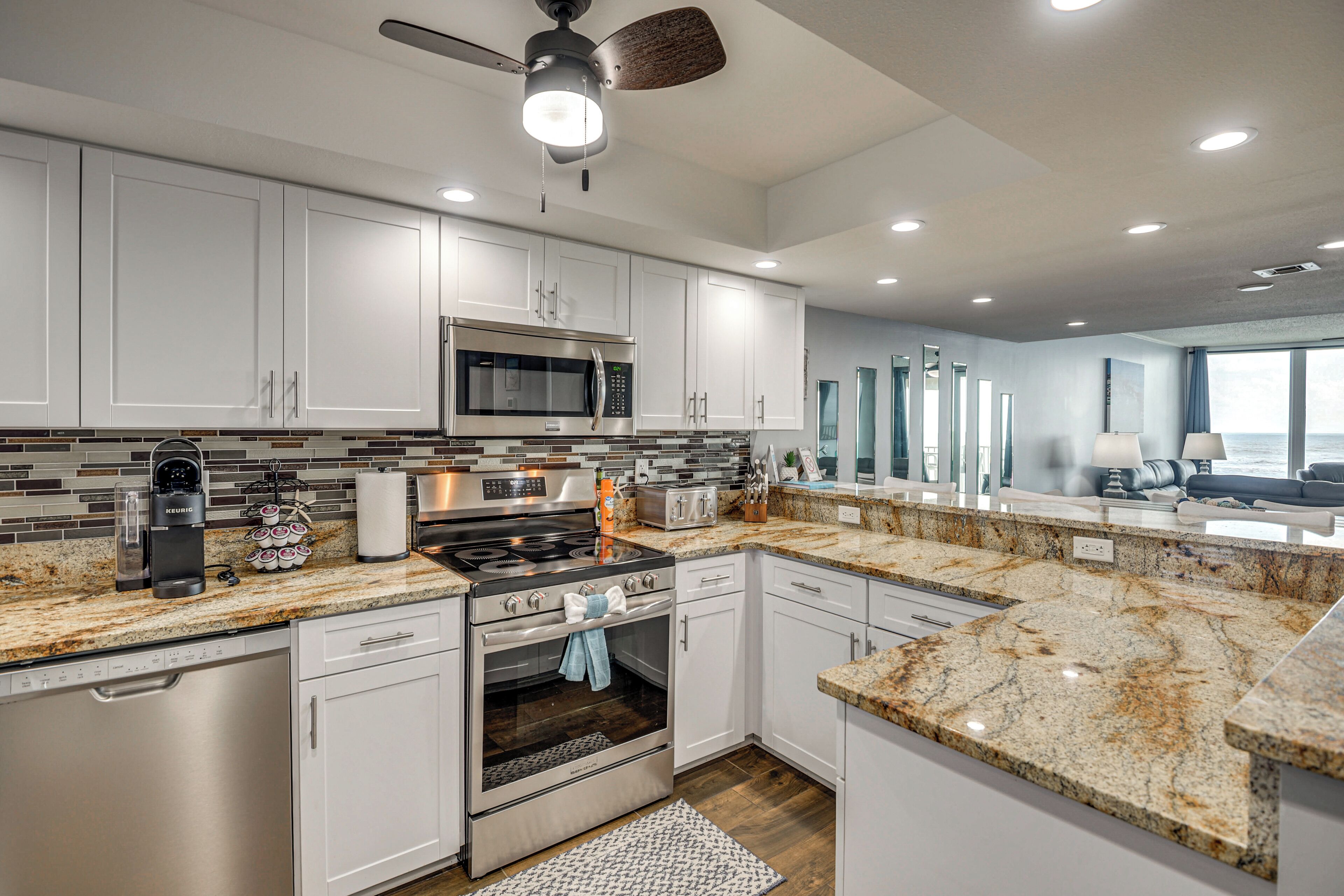 A modern kitchen with white cabinets, stainless steel appliances, a granite countertop, and a ceiling fan.