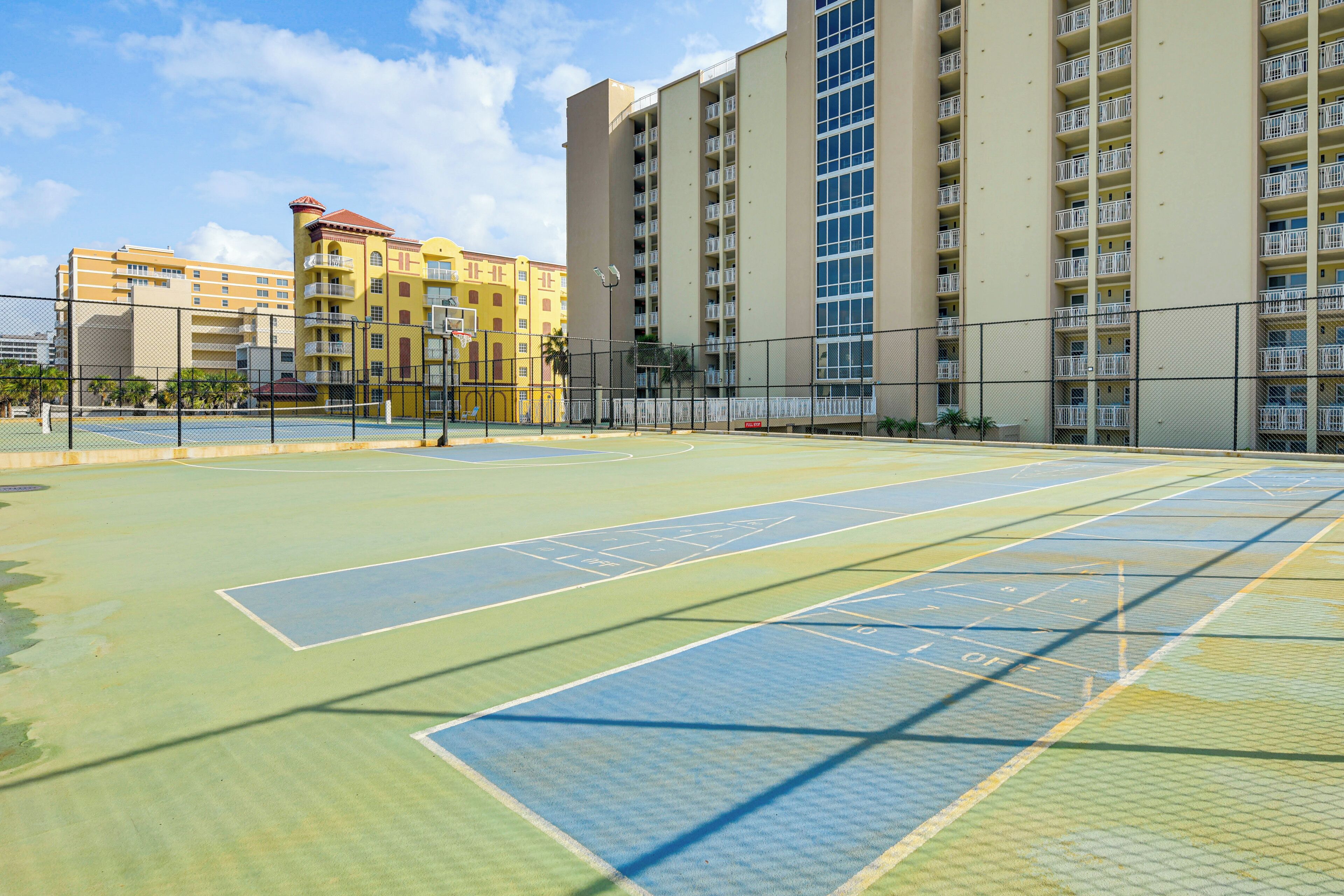 Cancha de tennis a l'aire lliure amb una tanca, envoltada d'edificis d'alguns pisos amb balcons.