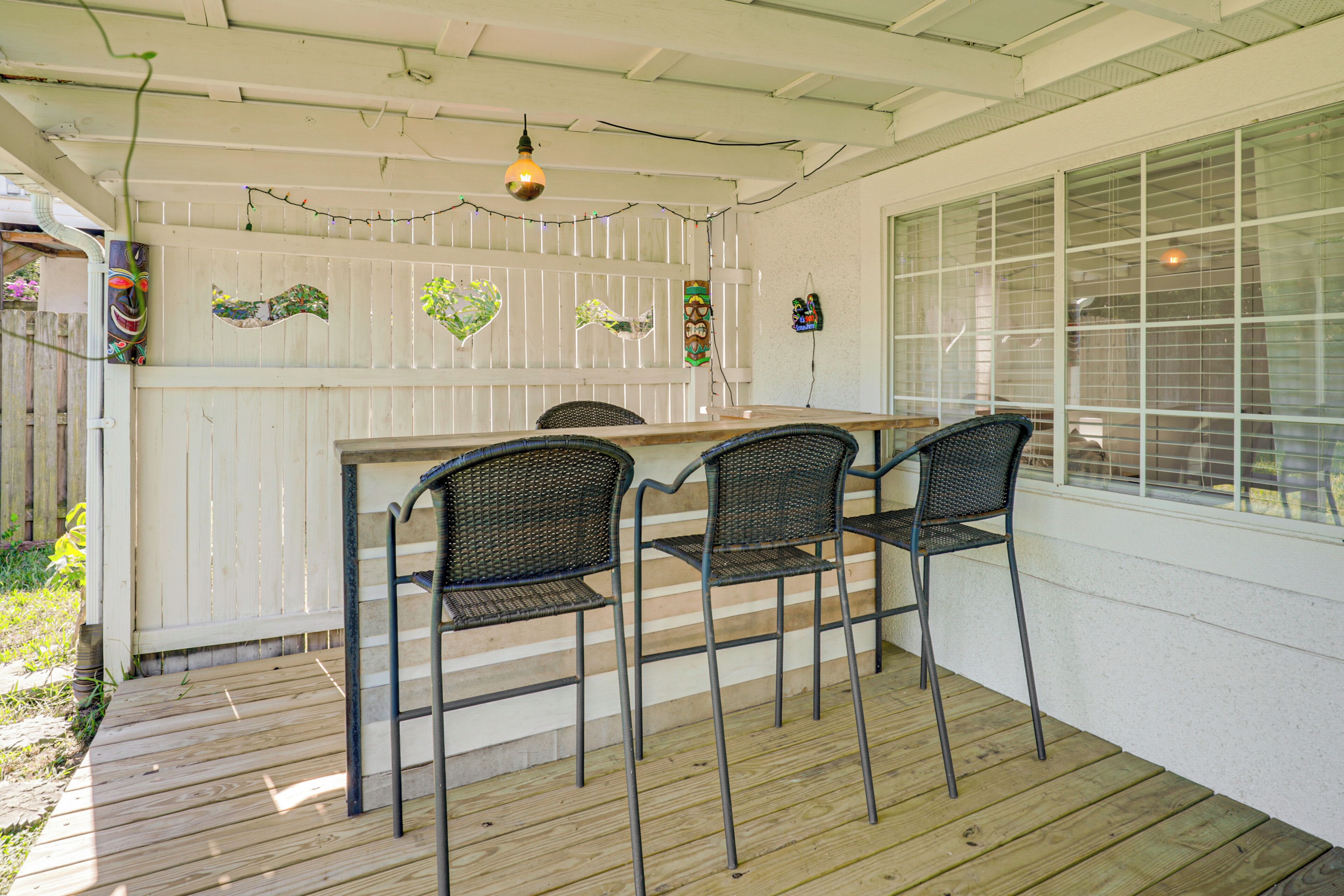 Un espace extérieur abrité, doté d’une terrasse en bois, de chaises en métal et d’une clôture blanche agrémentée d’éléments décoratifs.