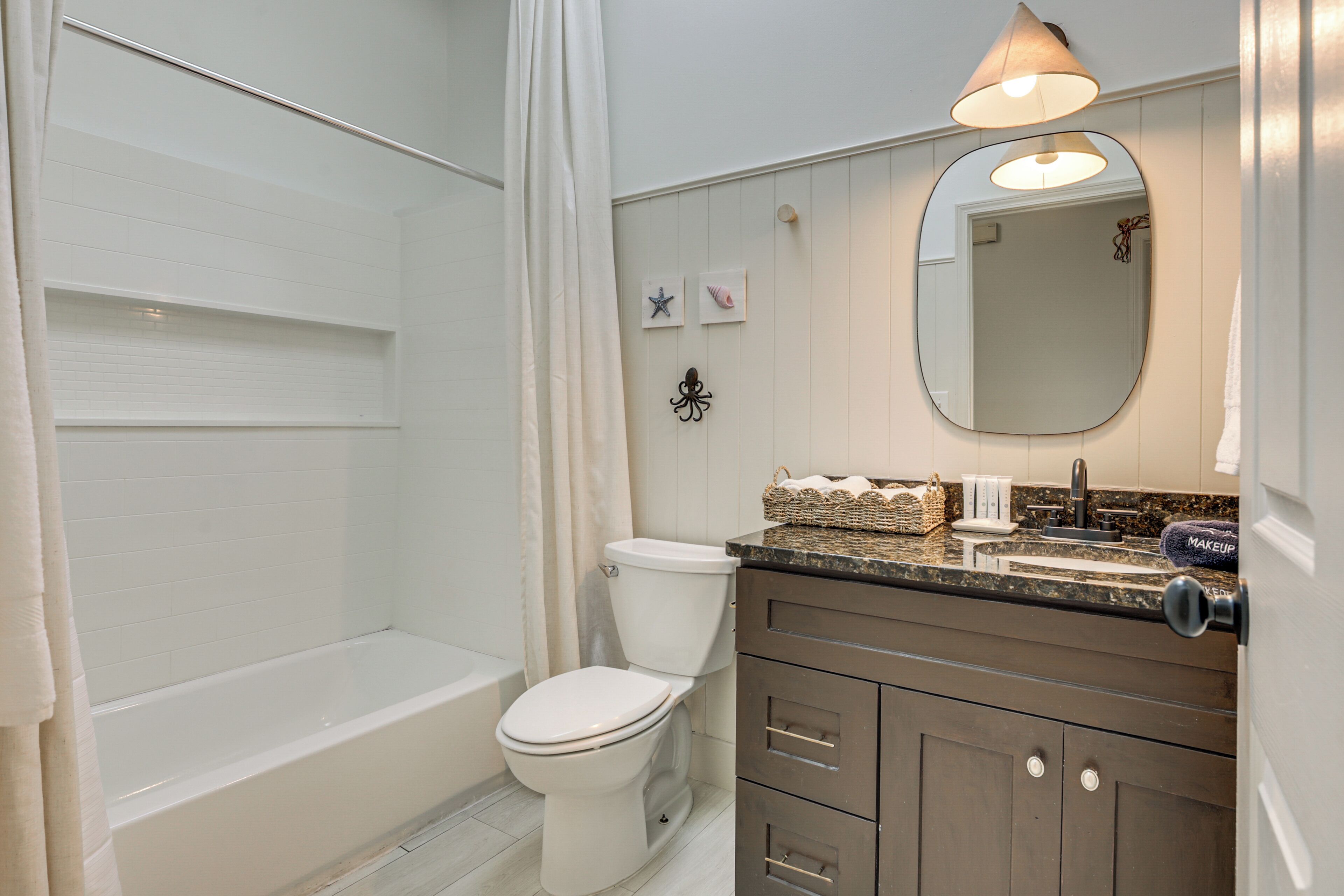 A bathroom with a bathtub, toilet, vanity with a mirror, and a shower curtain.