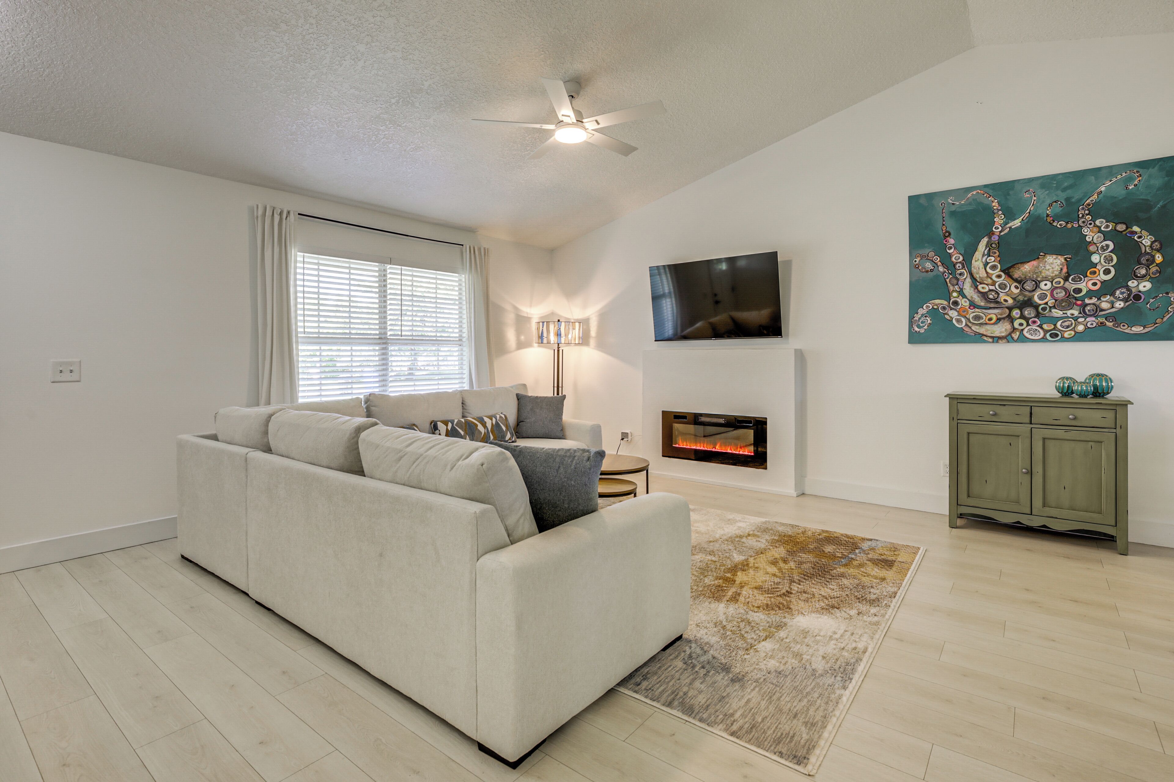 A living room with a sofa, a fireplace, a ceiling fan, and a painting on the wall.