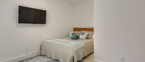 Un dormitorio con una cama, un televisor instalado en la pared y una alfombra estampada.