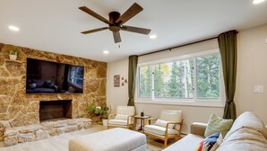 A living room with a stone fireplace, a flat-screen TV, and comfortable seating. - Hot Tub + Game Room: Peaceful Retreat in Evergreen (Evergreen)