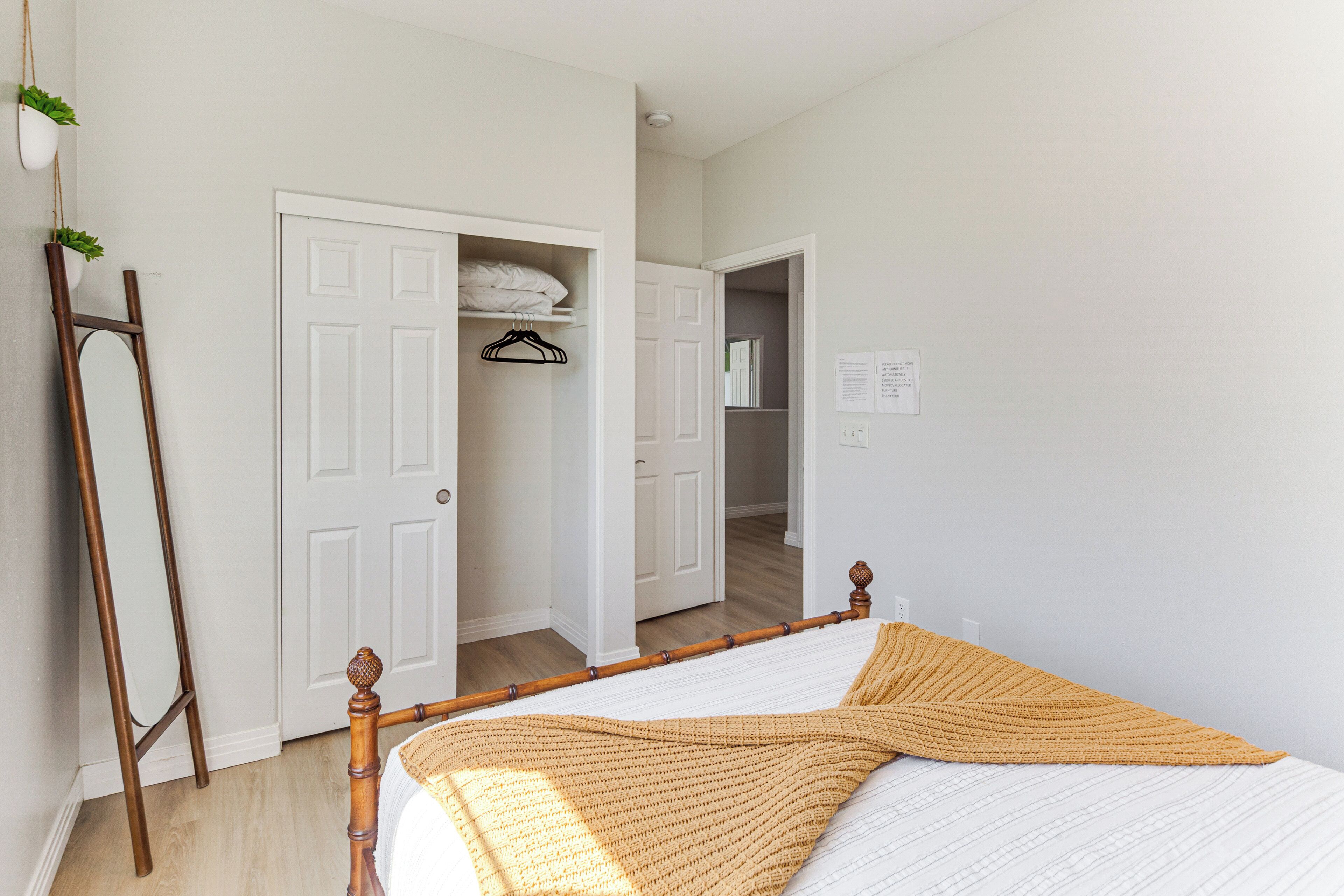 Een slaapkamer met een bed, houten vloer, witte muren, een witte deur en een witte kast.
