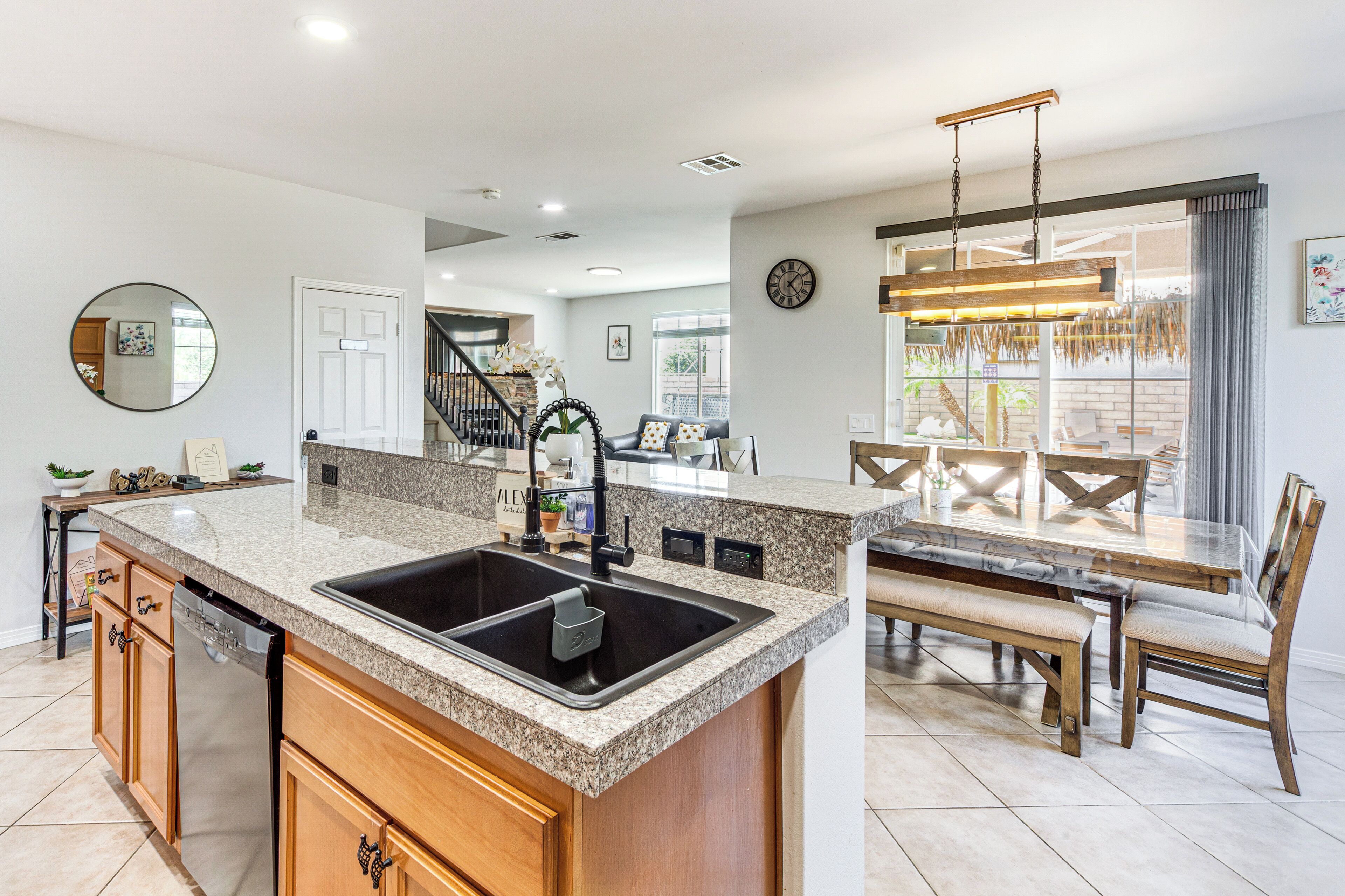 A modern kitchen with granite countertops, a black sink, wooden cabinets, and a dining area with a wooden table and chairs.