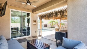 An outdoor patio with a ceiling fan, a glass door leading to a pool area, and a seating arrangement with a wooden table and cushions. - Relaxing Desert Oasis, 4 Mi to Coachella Festivals (Coachella)