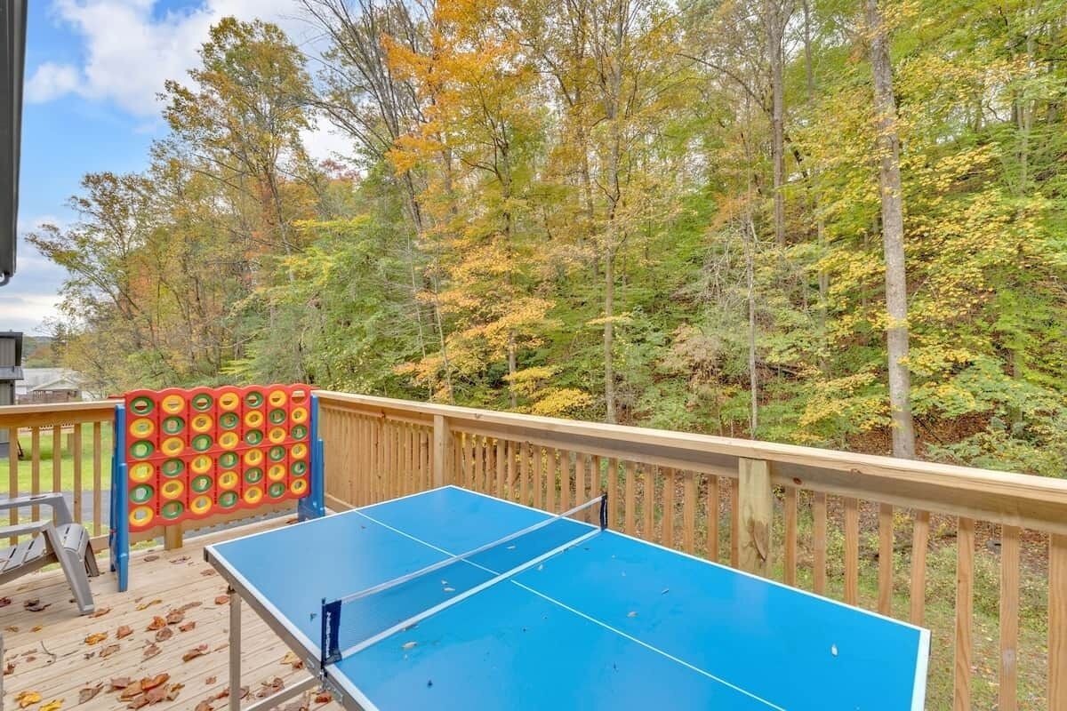 Une table de ping-pong sur une terrasse en bois, avec vue sur les arbres aux couleurs automnales.