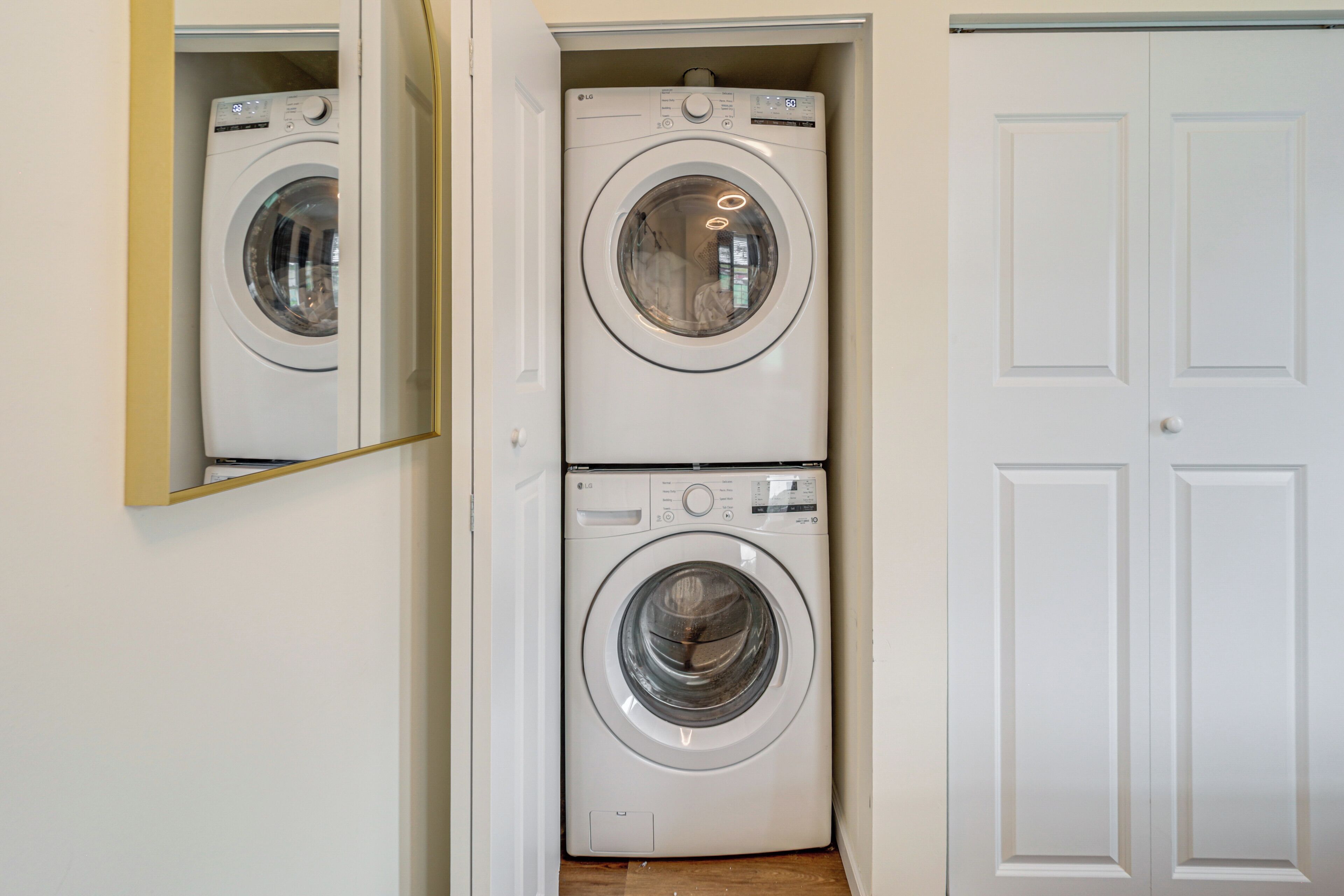 A laundry room with two stacked washing machines and a mirror on the left.