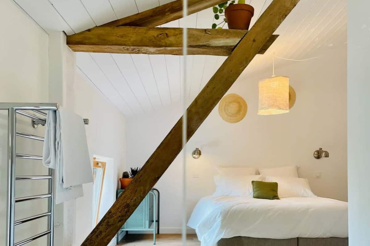 A bedroom with a sloped ceiling, a bed, a hanging light fixture, and a patterned floor.