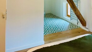 A room with a sloped ceiling, exposed wooden beams, a patterned floor, and a hanging light fixture. - Maison Monsieur Léger Maison de vacances (Montaut)