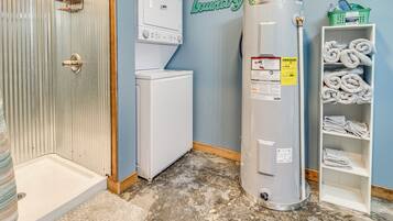 A laundry room with a water heater, a washing machine, and a shelf with towels.
