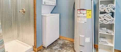 A laundry room with a water heater, a washing machine, and a shelf with towels.