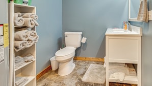 Baño con inodoro, lavabo y repisas con toallas.