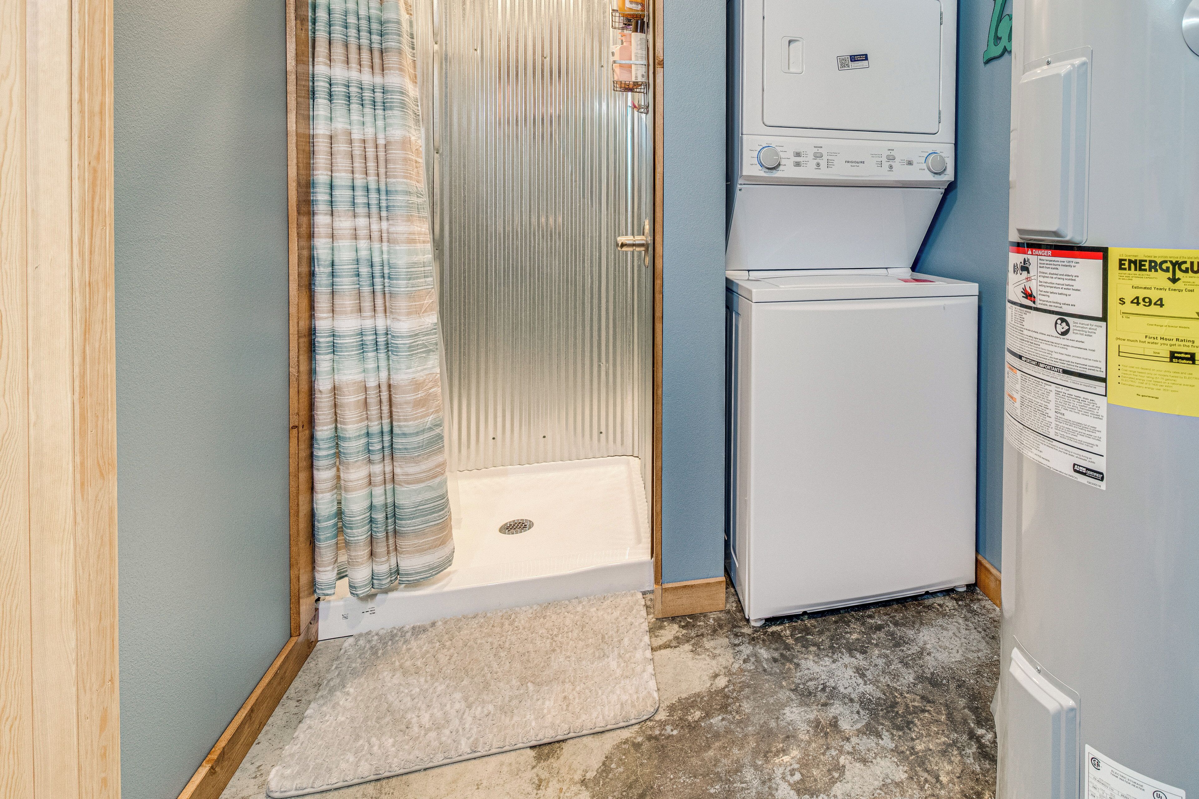 A small laundry room with a washing machine, dryer, and a shower area with a striped shower curtain.