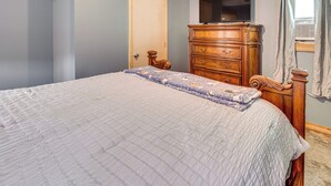 Un dormitorio con cama, cómoda de madera y televisor en la pared.
