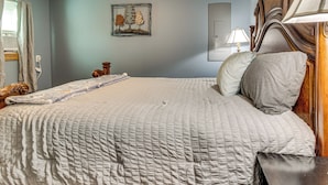 Una cama bien hecha con colcha blanca, cabecera de madera y mesita de noche con lámpara.