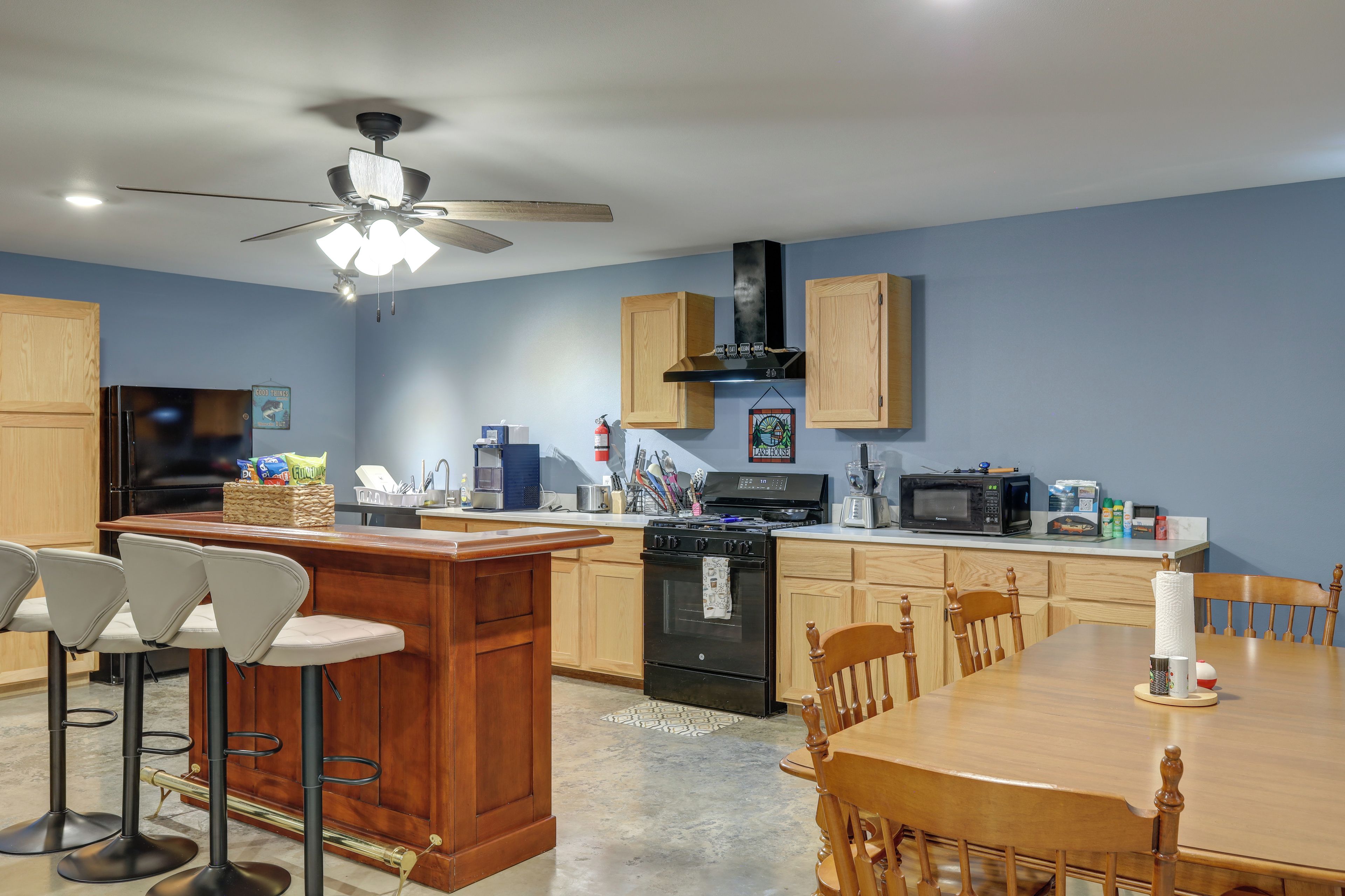 A modern kitchen with a central island, wooden cabinets, a black stove, and a ceiling fan.