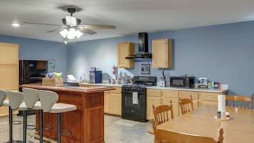 A modern kitchen with a central island, wooden cabinets, a black stove, and a ceiling fan.