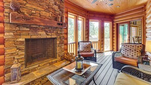 A log cabin interior with a stone fireplace, wicker furniture, and large windows. - Hike, Fish & More: Grand Cabin w/ Decks in Sturgis (Sturgis)