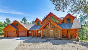 A log cabin with a stone foundation, multiple garage doors, and a gravel driveway. - Hike, Fish & More: Grand Cabin w/ Decks in Sturgis (Sturgis)