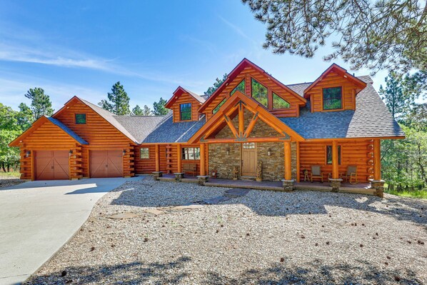 A log cabin with a stone foundation, multiple garage doors, and a gravel driveway. - Furnished Decks & Game Room: Sturgis Rally Cabin (Sturgis)