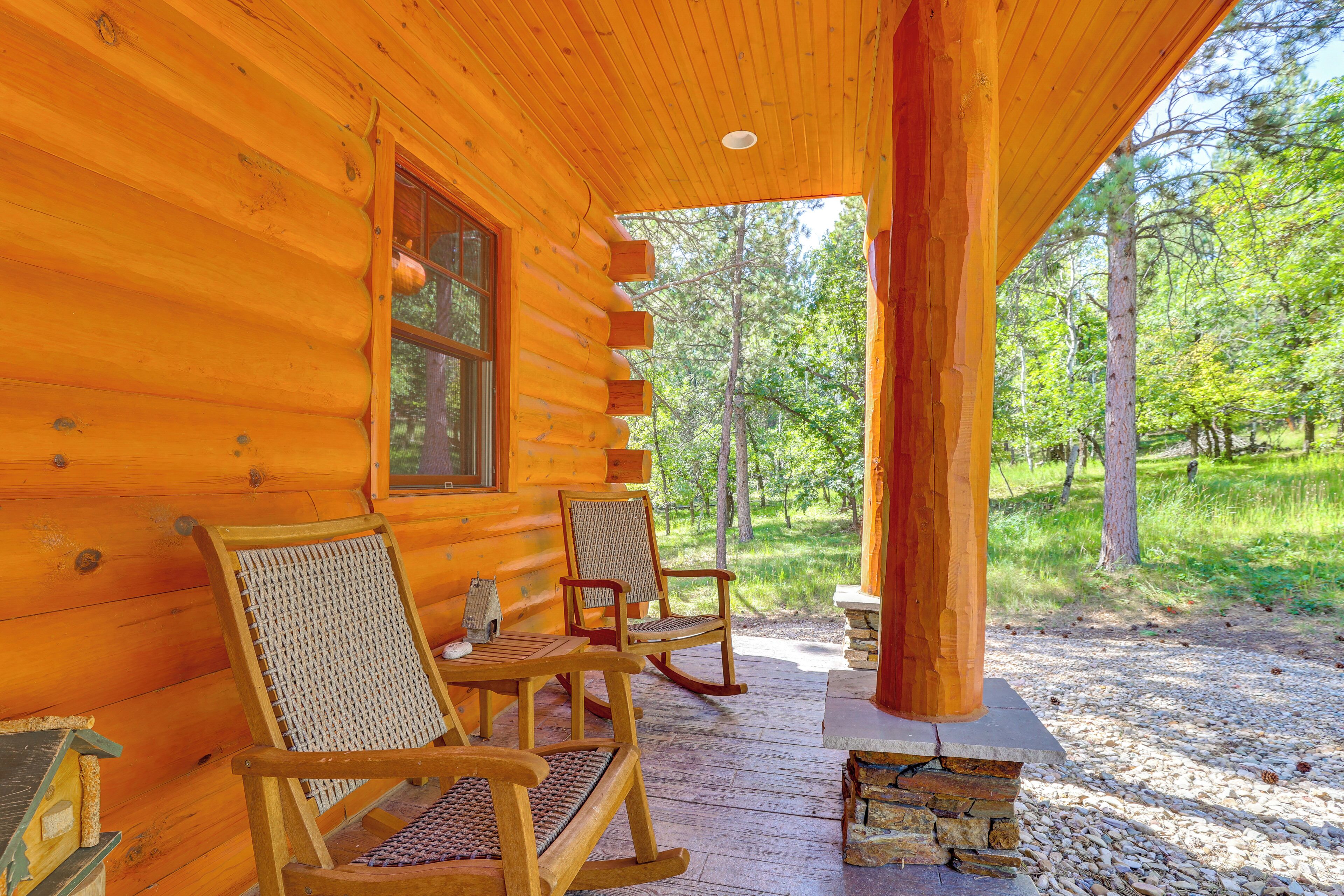 A log cabin with a porch, two rocking chairs, and a stone fireplace.
