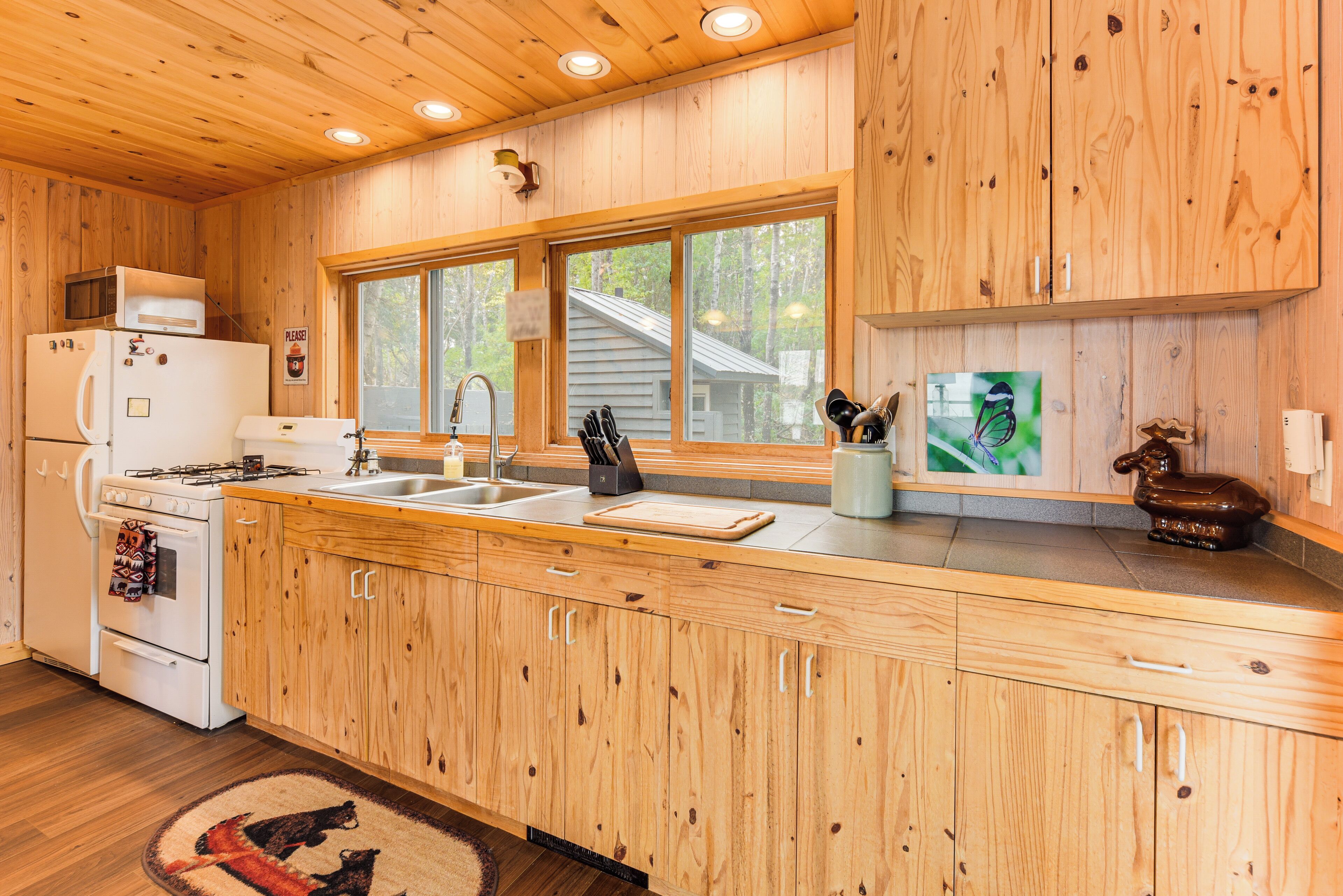Une cuisine rustique aménagée dans une cabane en bois, avec un poêle, un évier et de grandes fenêtres.